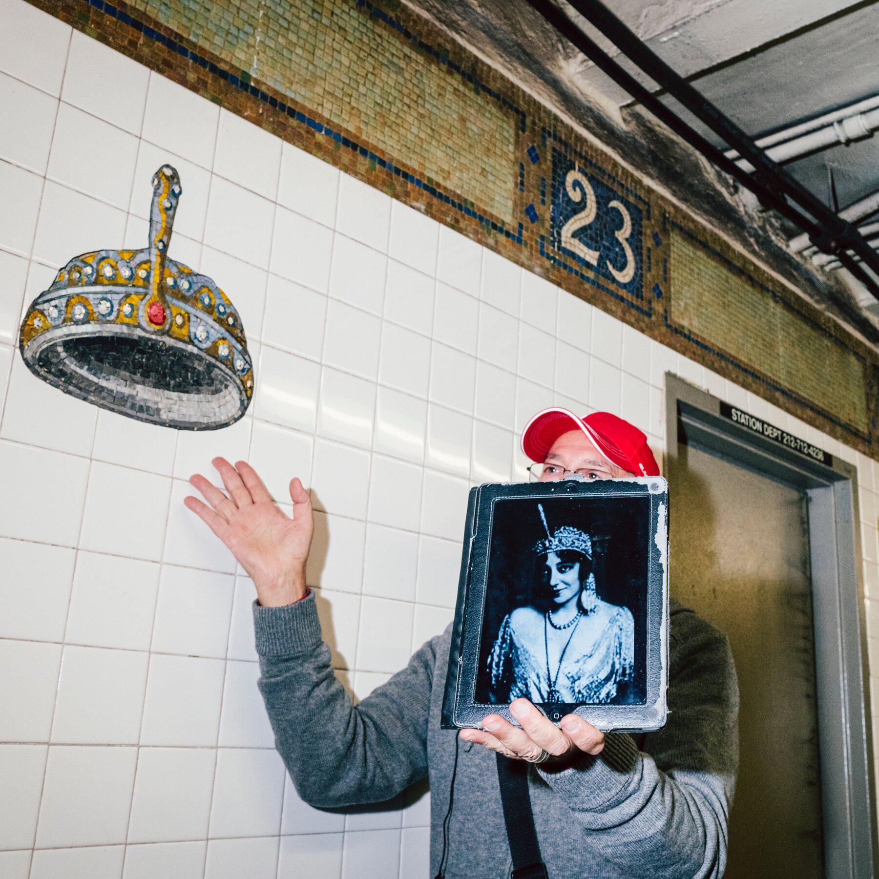 A tour guide points to a mosaic by the artist Keith Goddard that pays homage to famous hats.