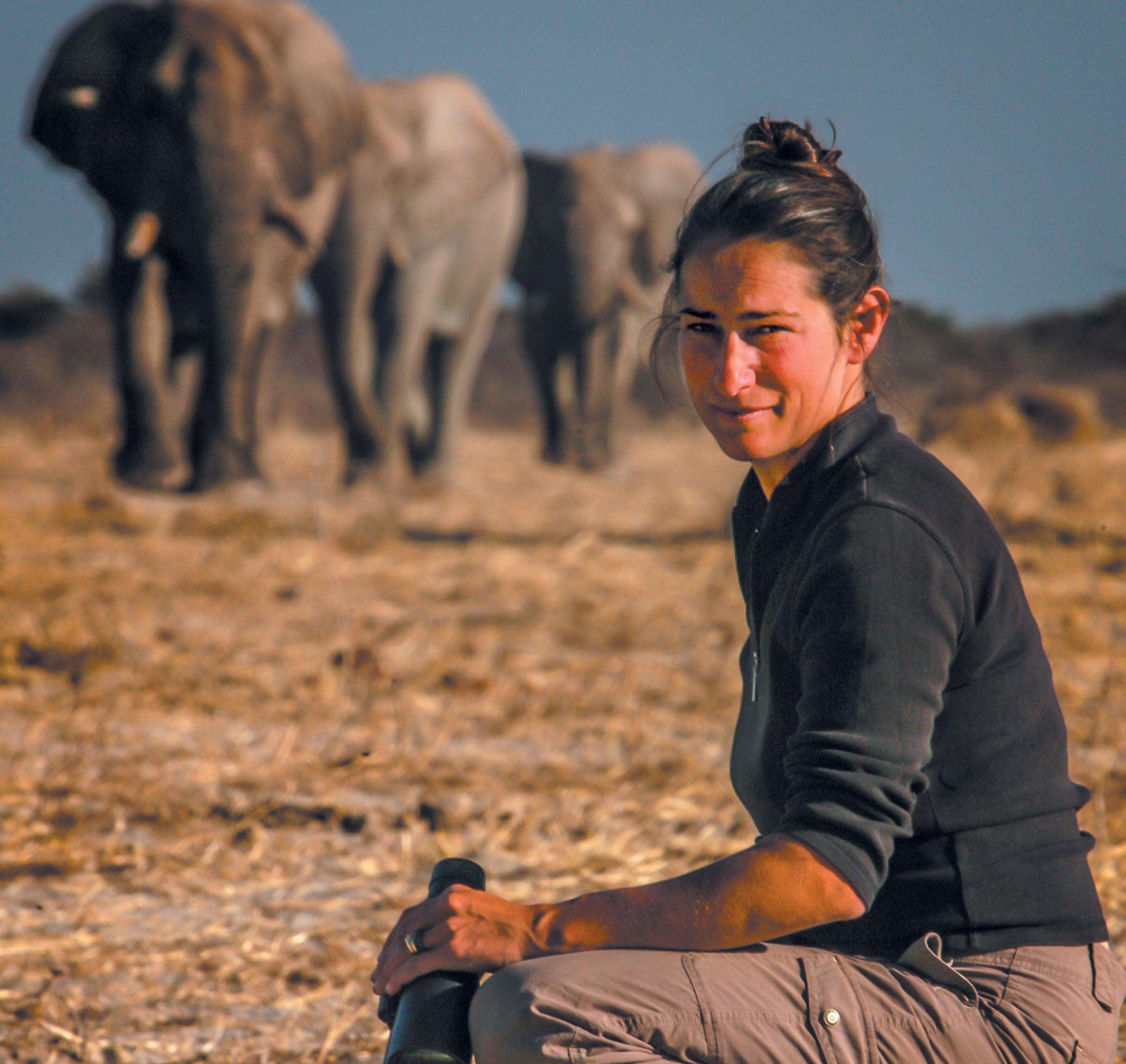 Caitlin O'Connell squatting with three elephants in the background