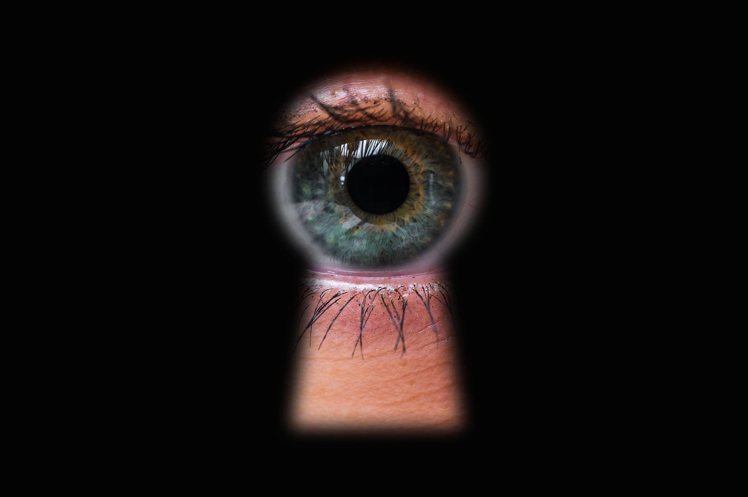 Human eye looking through a keyhole directly toward the camera