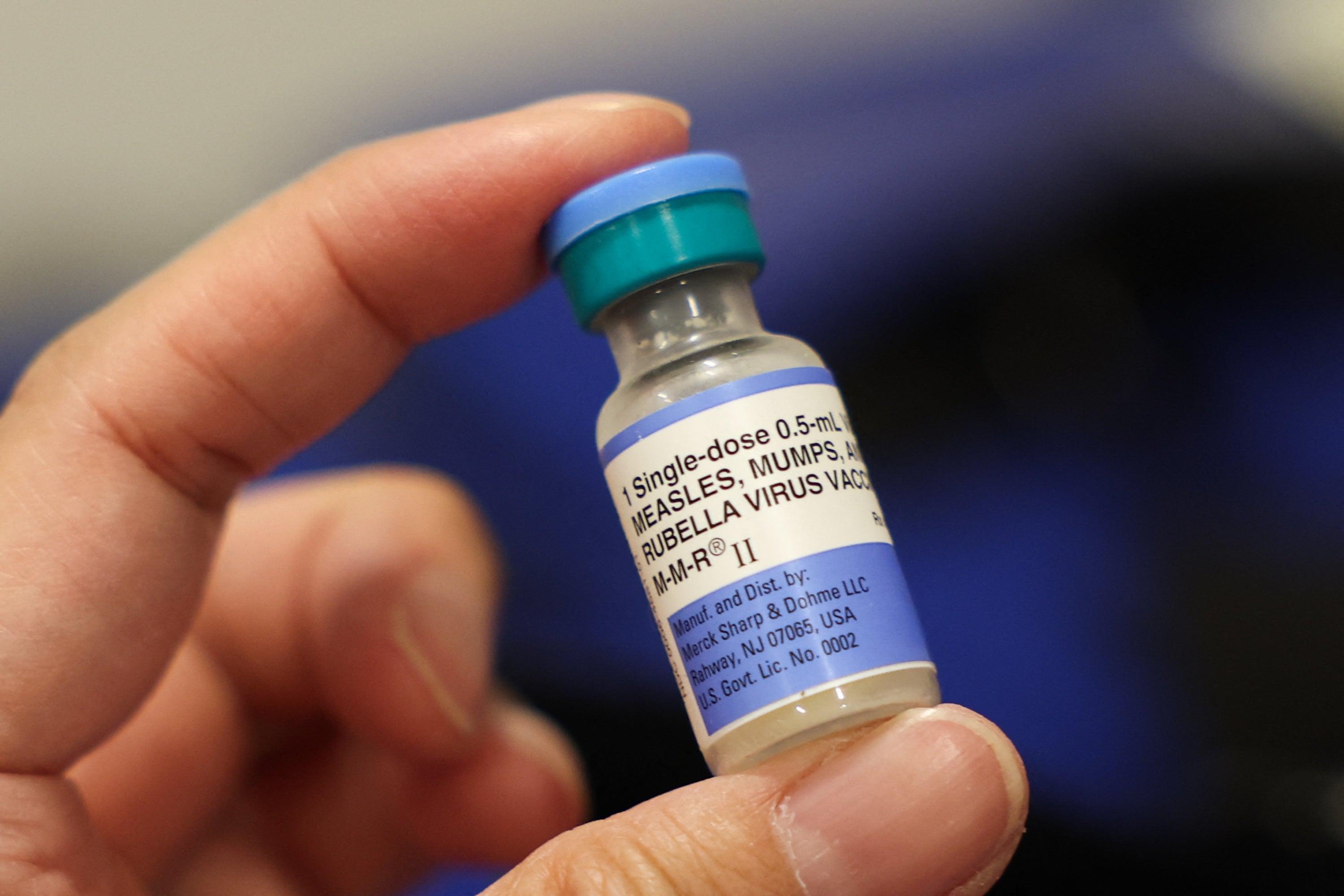A hand holding a vial of Measles, Mumps and Rubella vaccine.