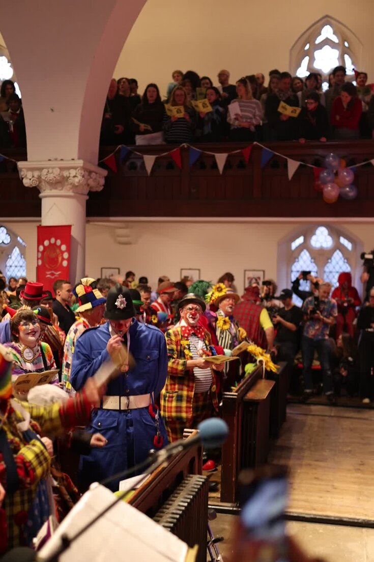 Clowns and other attendees singing at a service honoring Joseph Grimaldi at All Saints Church in London.